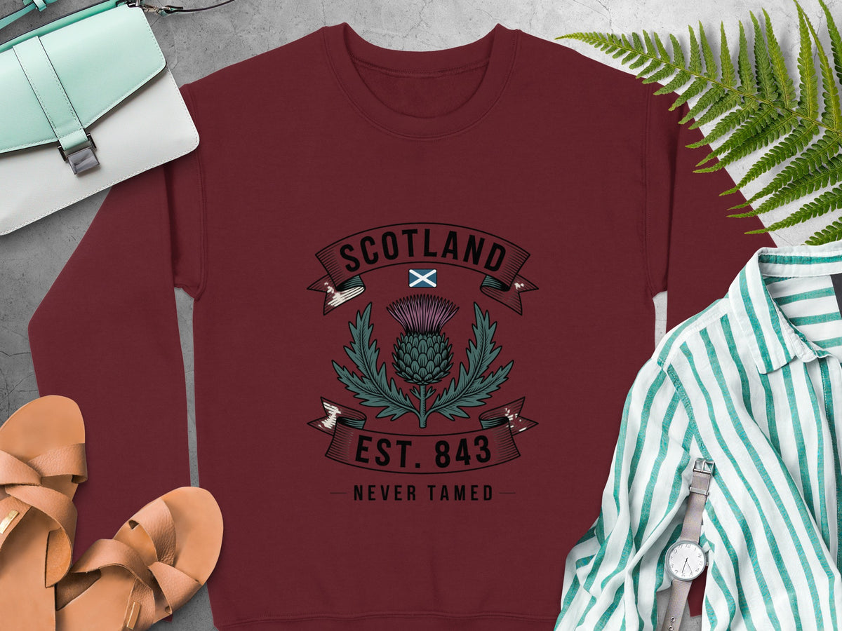 Burgundy sweatshirt with Scotland thistle design and "Est. 843 Never Tamed" text.