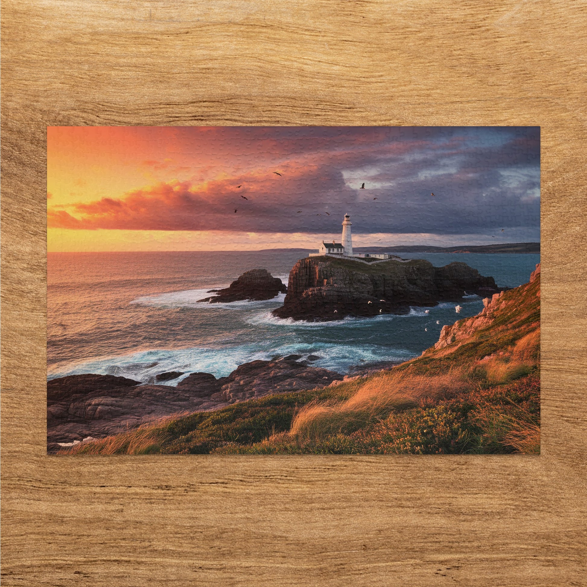White lighthouse on rocky island with birds flying during a dramatic sunset.