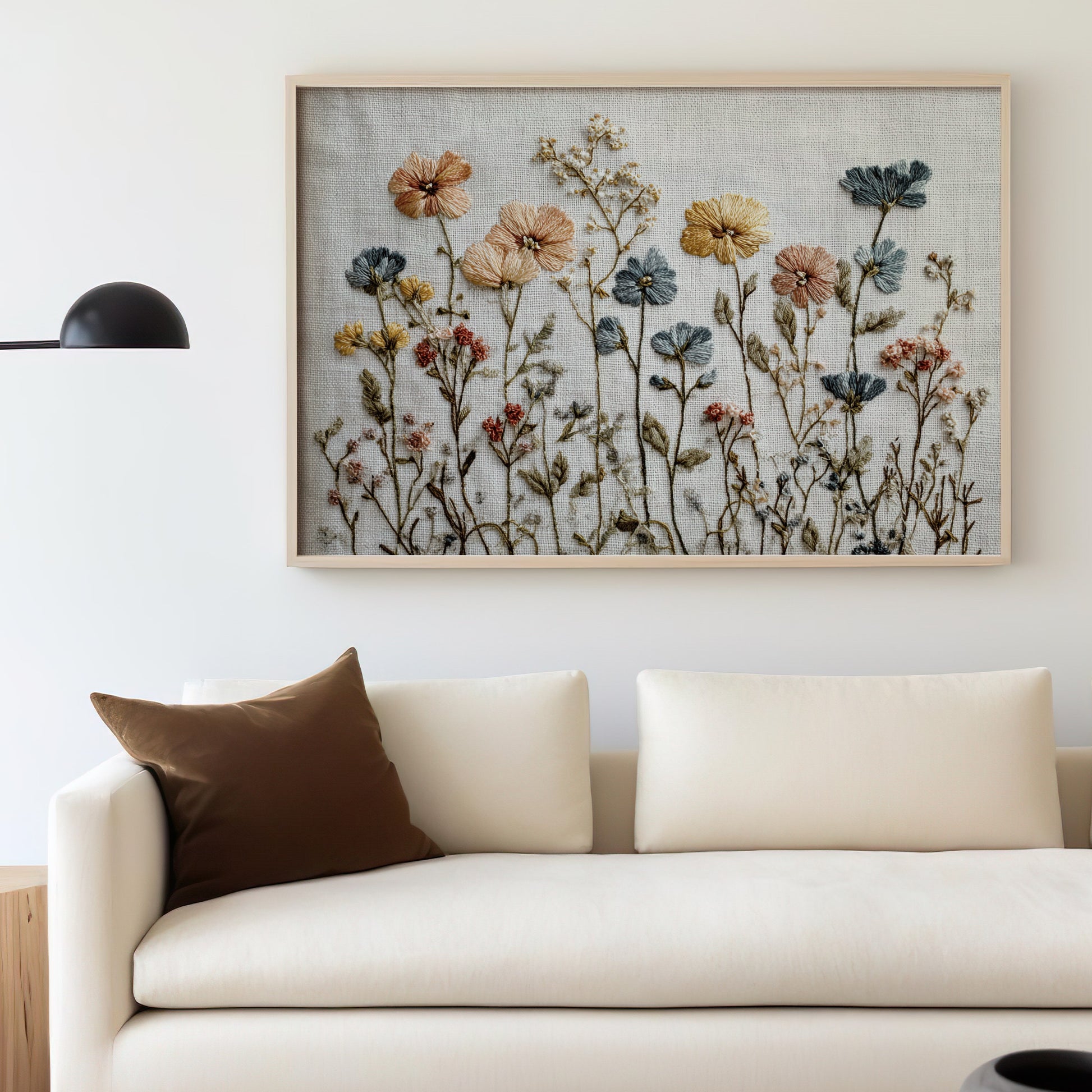 Framed floral embroidery art above a cream sofa with a brown throw pillow.