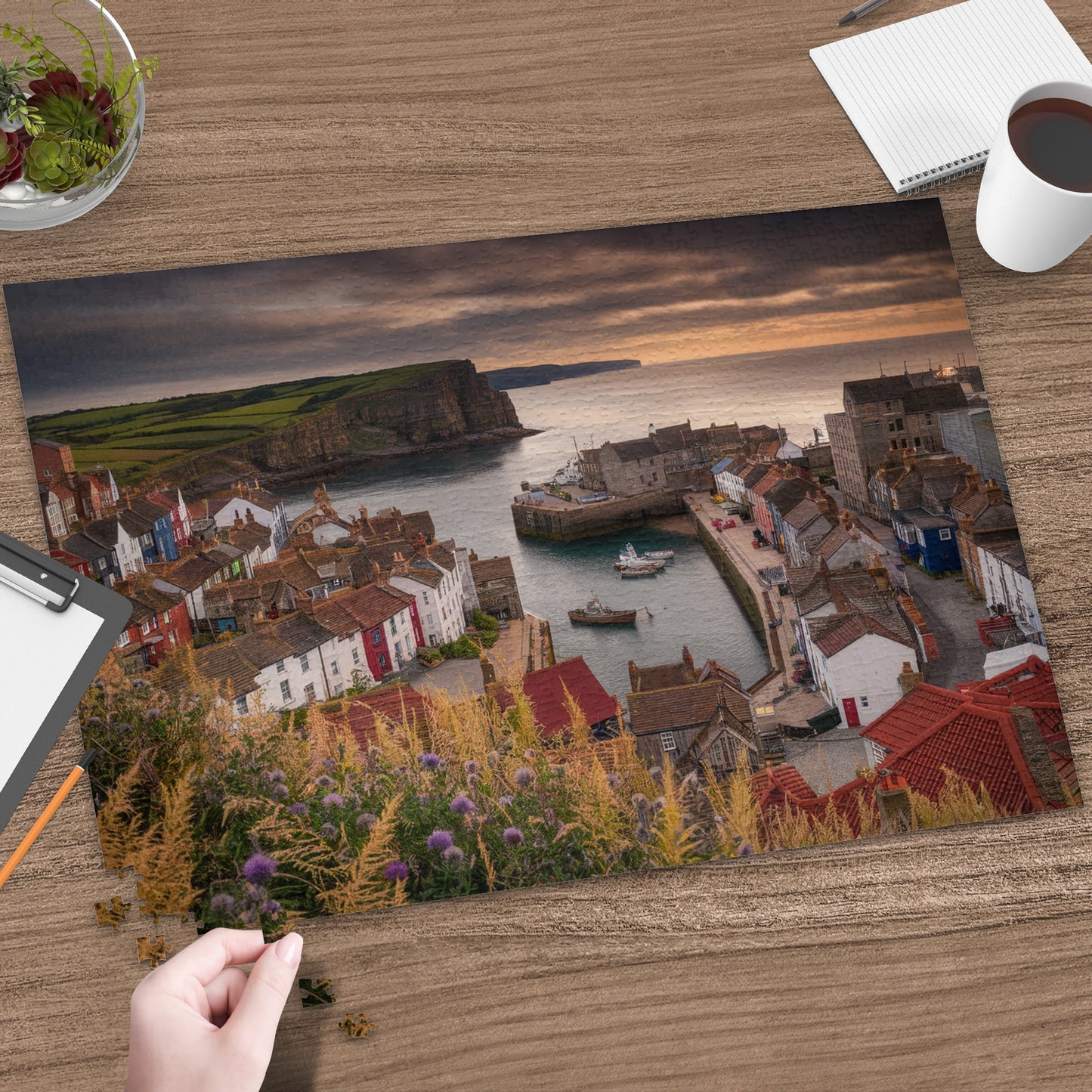 Colorful buildings line a harbor with boats against a dramatic sunset and cliff backdrop.