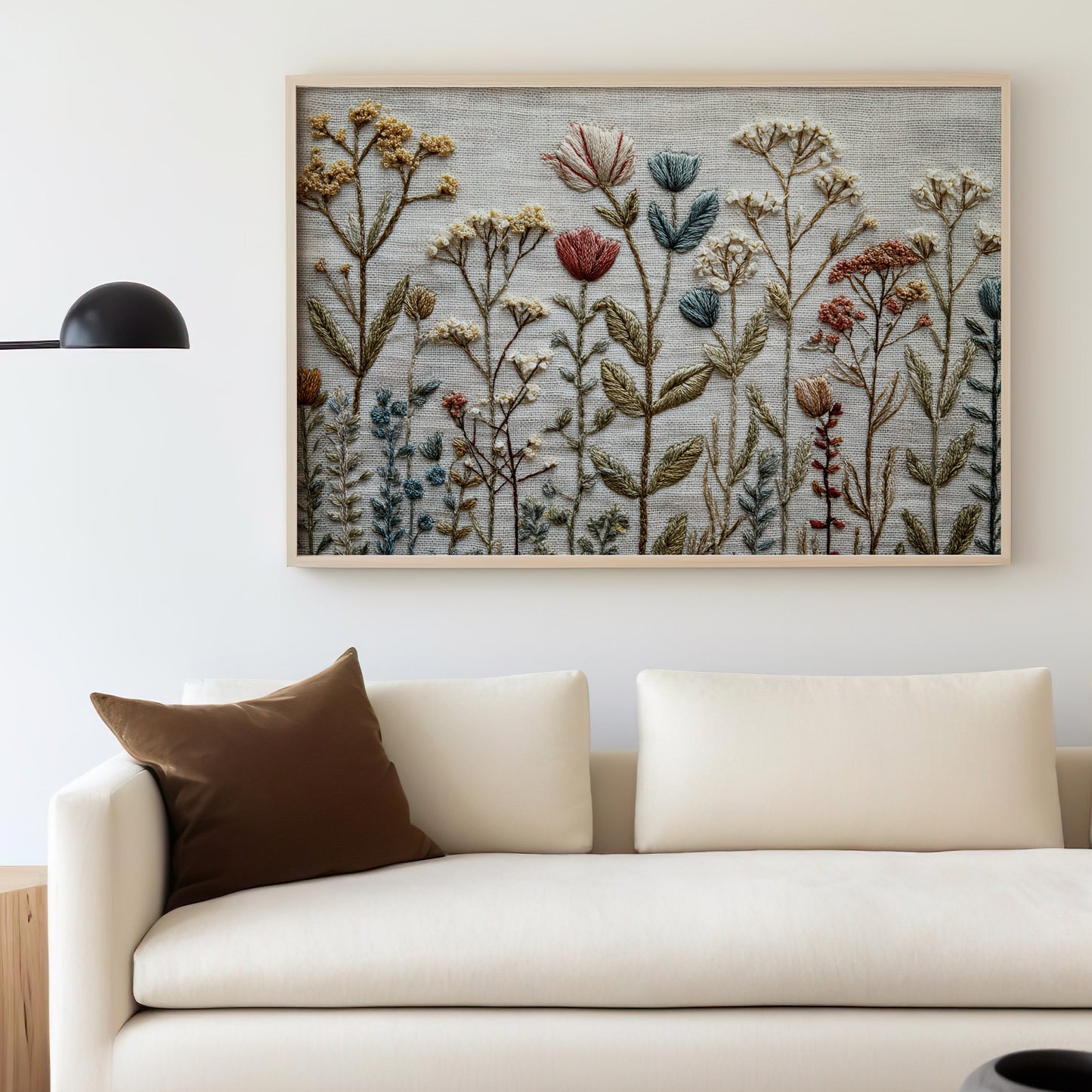 Embroidery art of wildflowers above a cream sofa with a brown throw pillow.