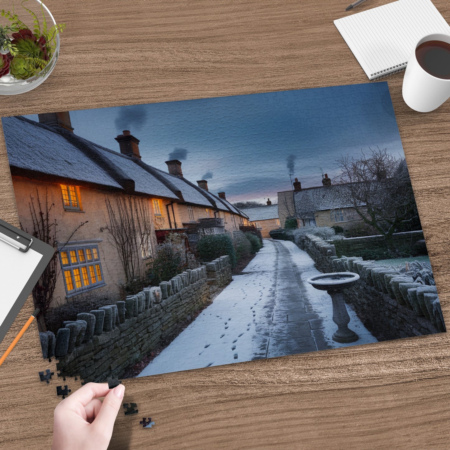 Snowy village lane with stone walls, thatched cottages, and chimney smoke at dusk.