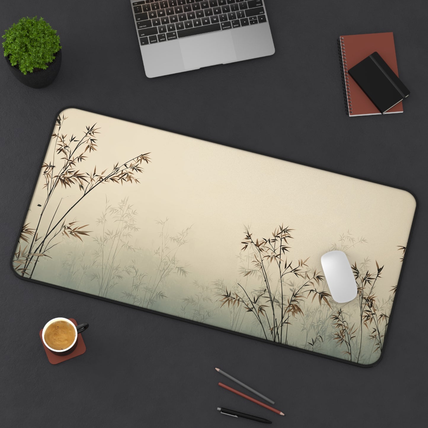 Desk setup with a large mouse pad featuring bamboo design, laptop, phone, and office supplies on a dark surface.
