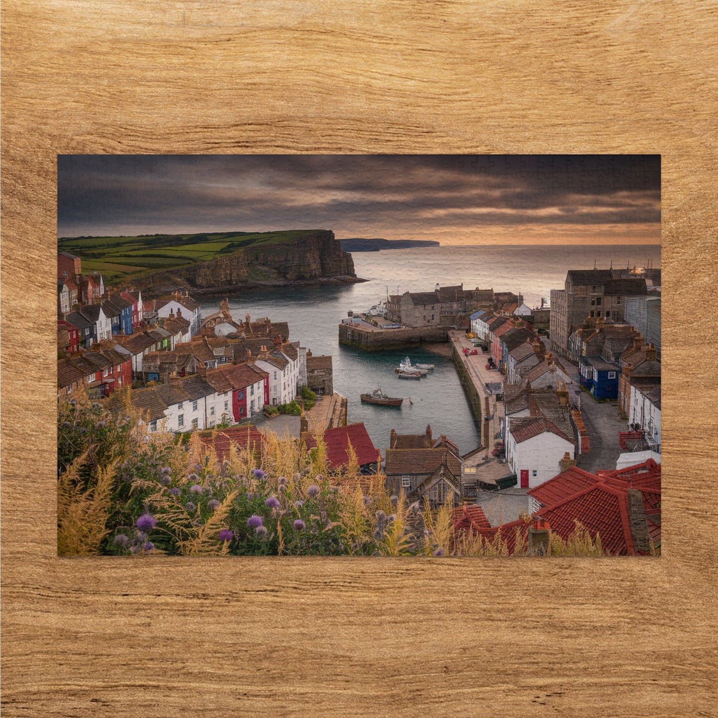 Harbor town with colorful houses, boats, cliffs, and moody sky.