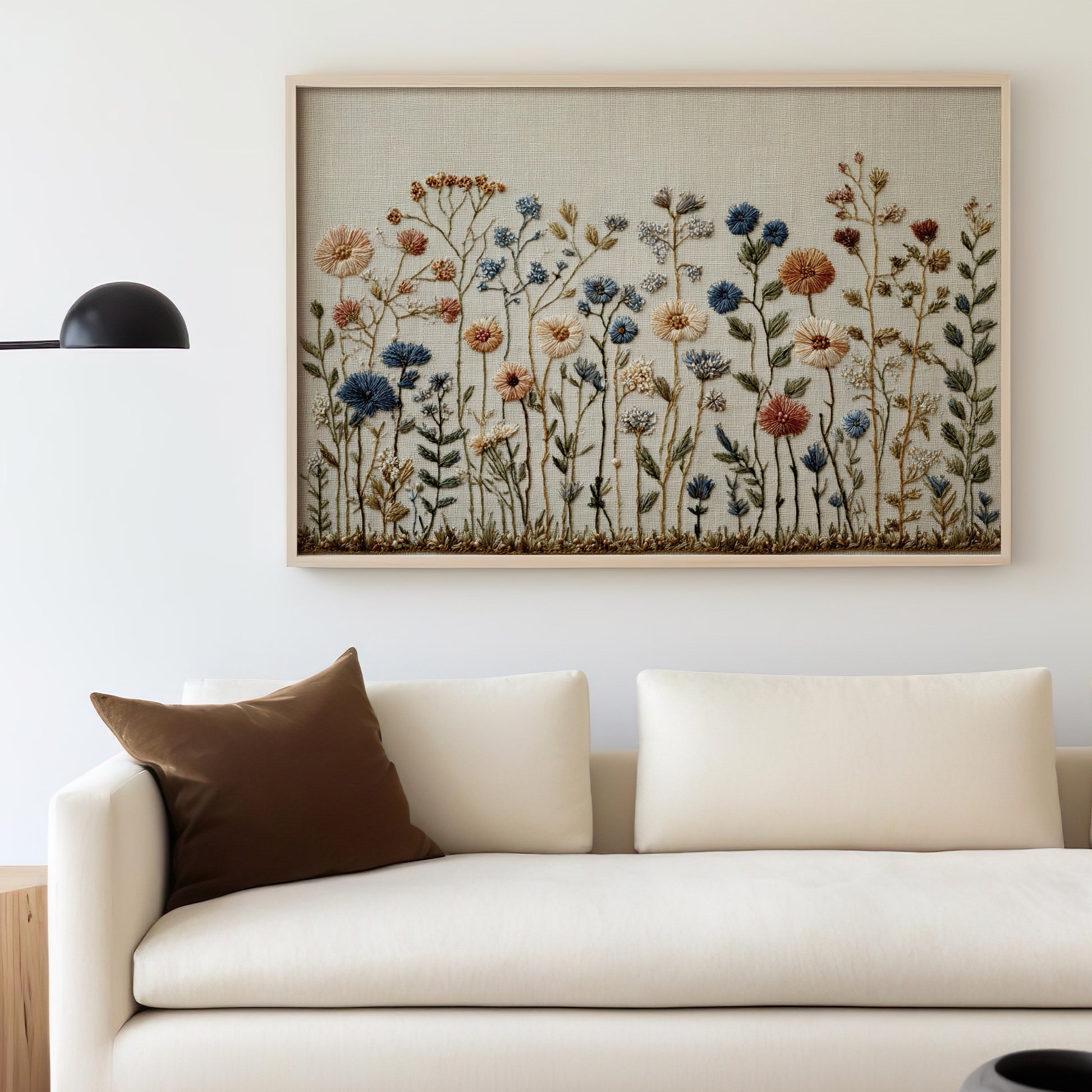 Embroidered floral artwork above a cream sofa with a brown throw pillow.