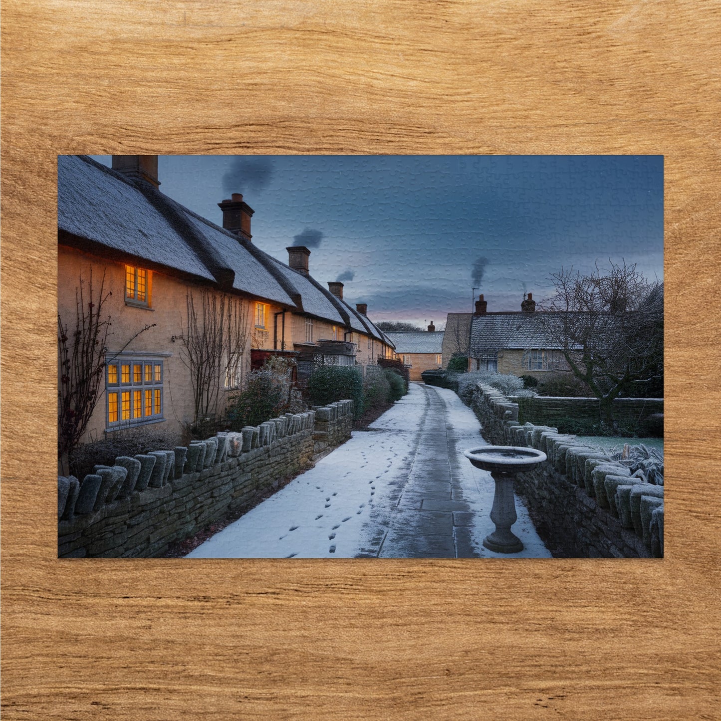 Snowy village lane lined with thatched-roof cottages and stone walls at dusk.