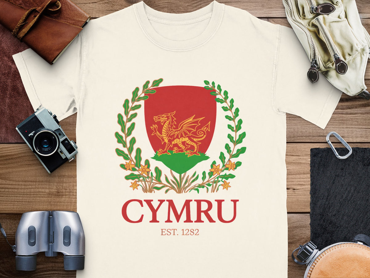 Cream t-shirt with a red shield featuring a golden dragon, green wreath, and text "CYMRU EST. 1282".