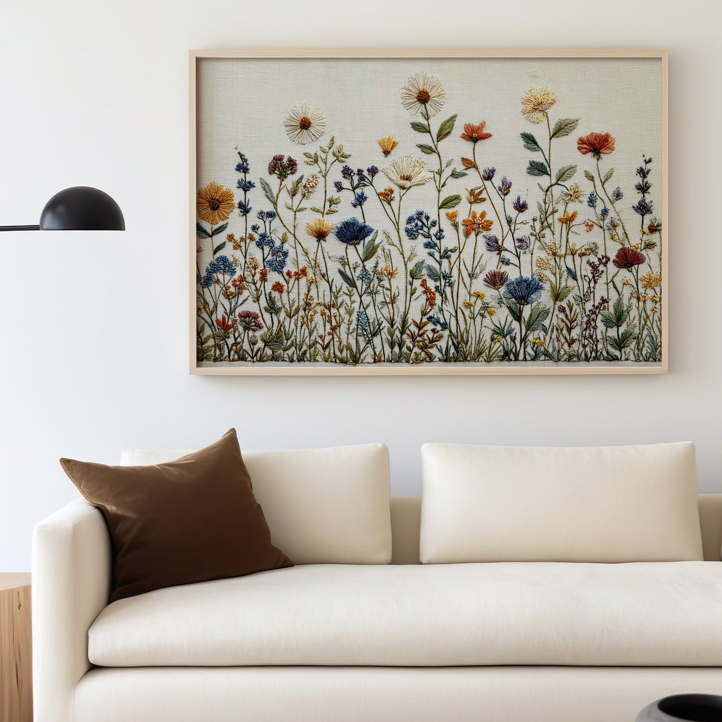 Embroidery art of wildflowers above a cream sofa with a brown pillow.