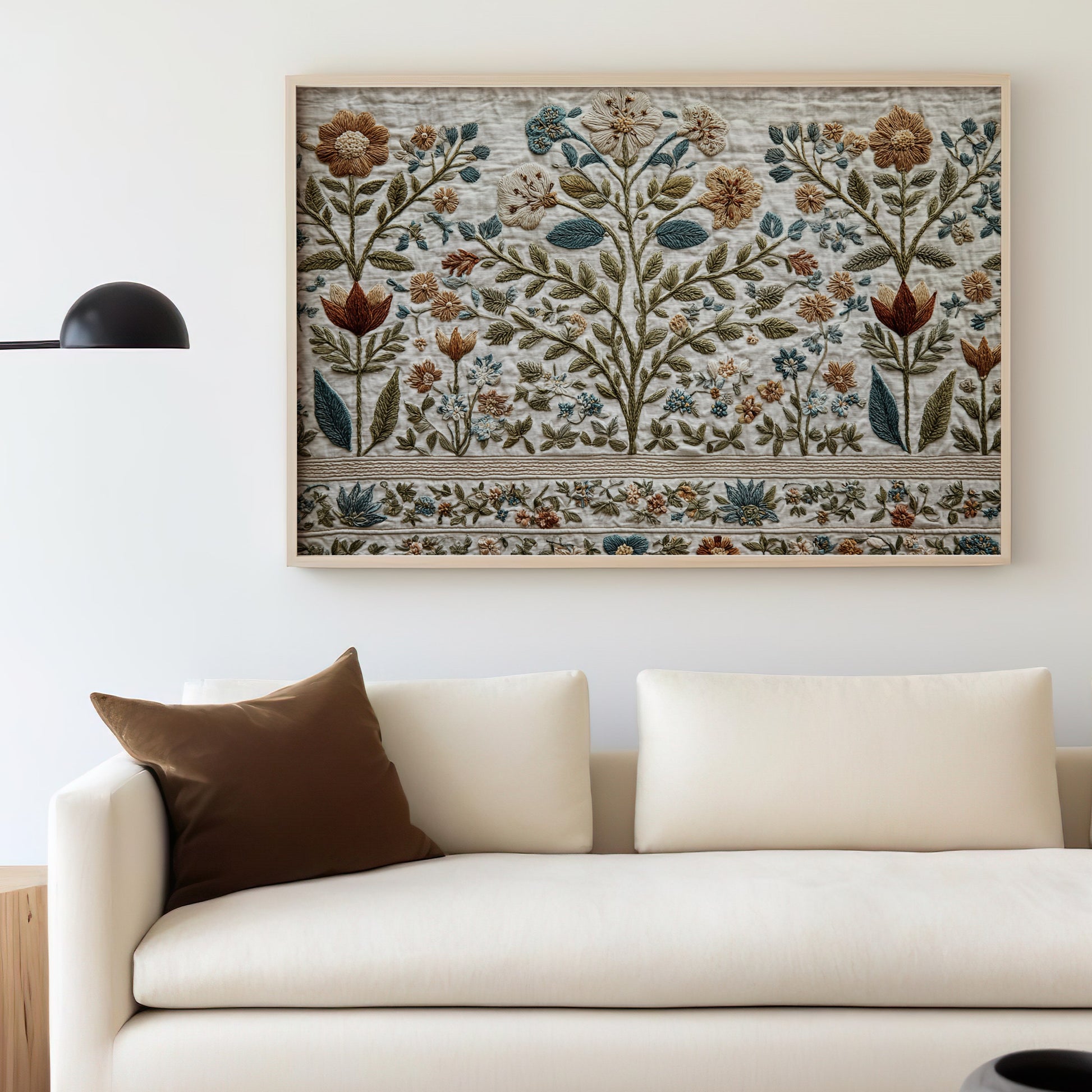Embroidered textile art depicting a floral tree motif hangs above a cream sofa.