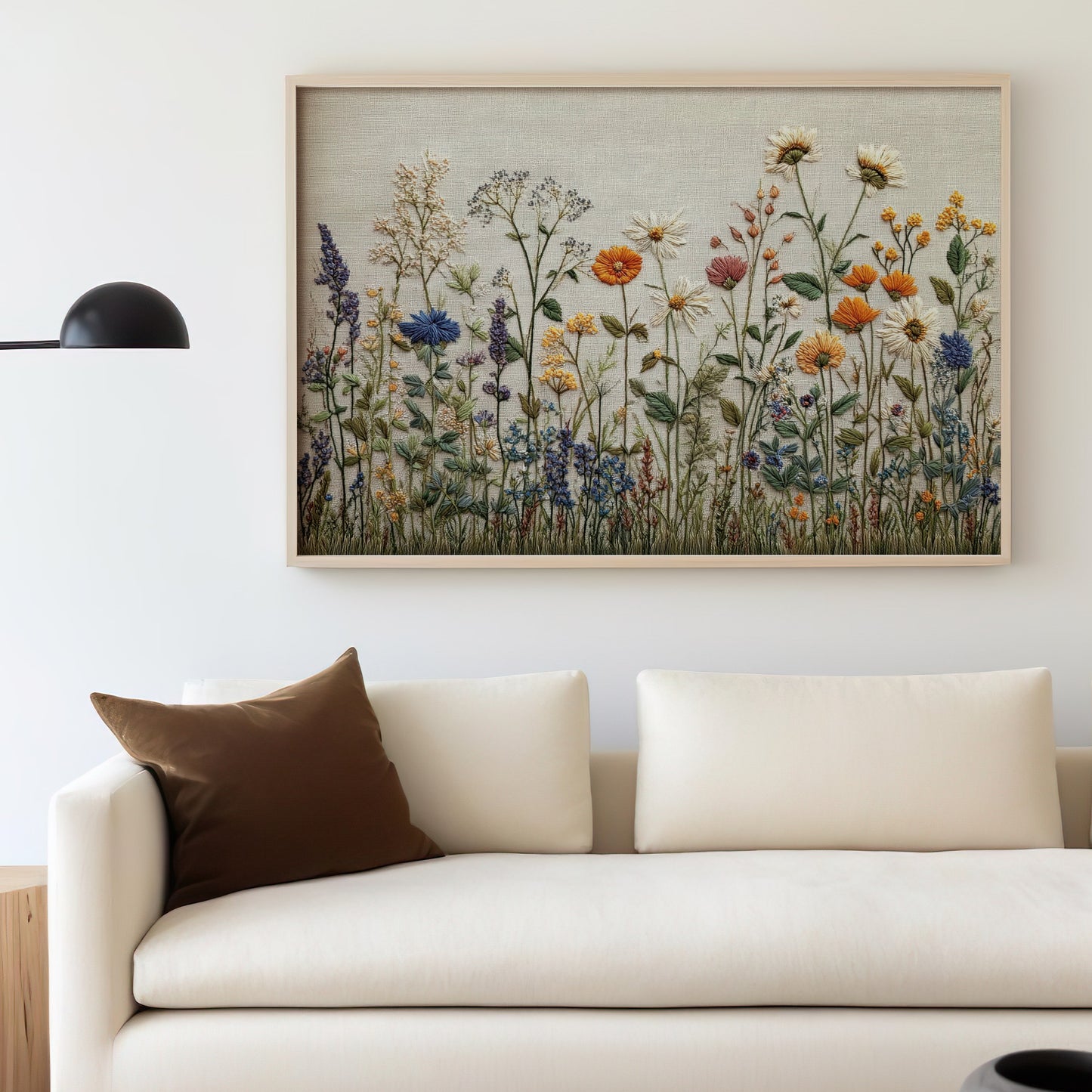 Embroidered framed artwork depicting a field of wildflowers above a cream sofa.