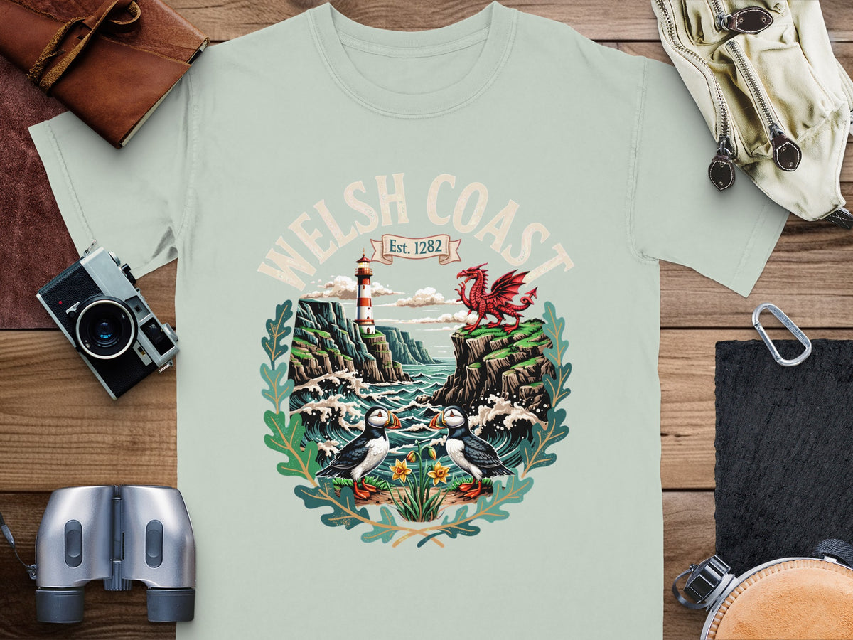 T-shirt graphic of Welsh Coast Est. 1282 with puffins, lighthouse, dragon, and cliffs.