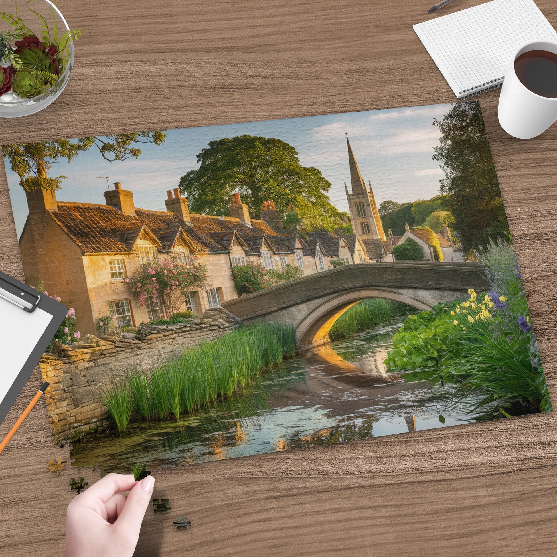 Quaint English village with stone bridge over a canal, cobblestone street, and church steeple.