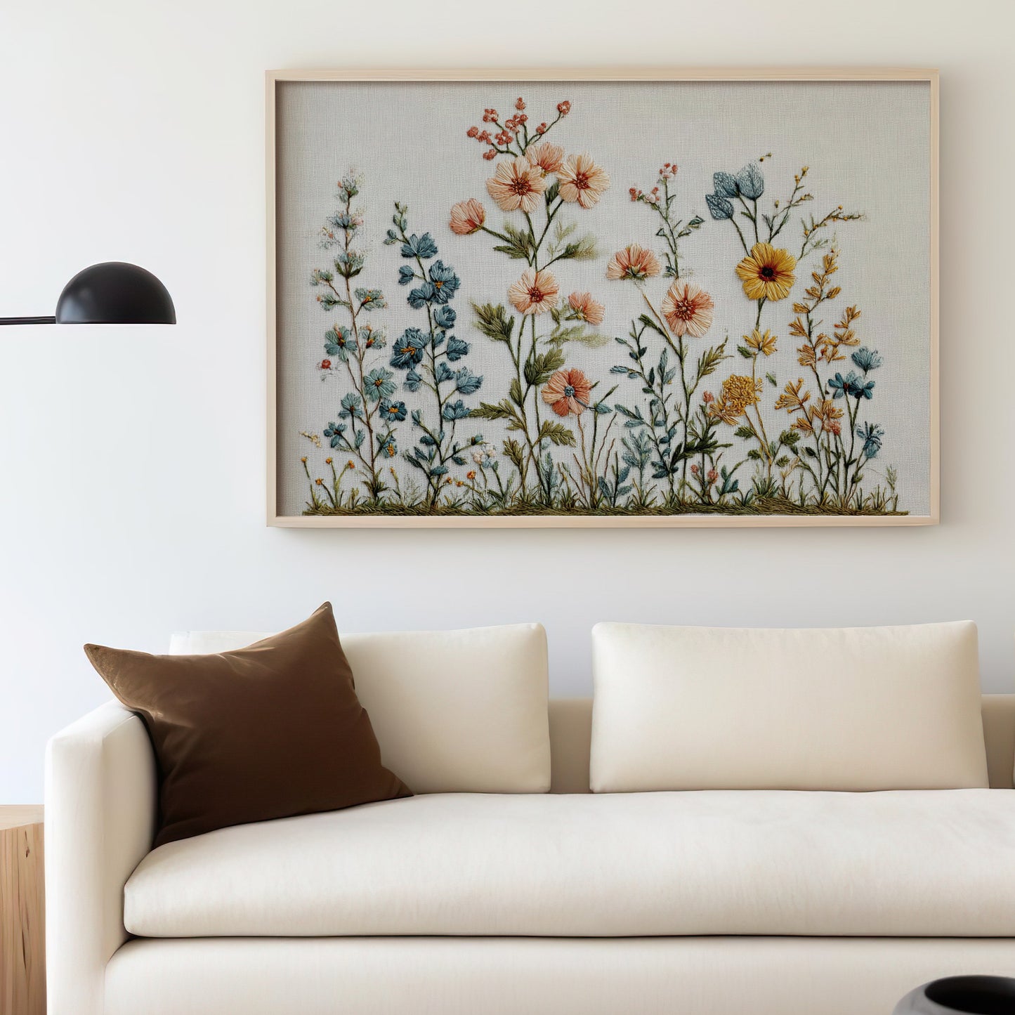 Embroidery art of wildflowers in a light wood frame above a cream sofa.
