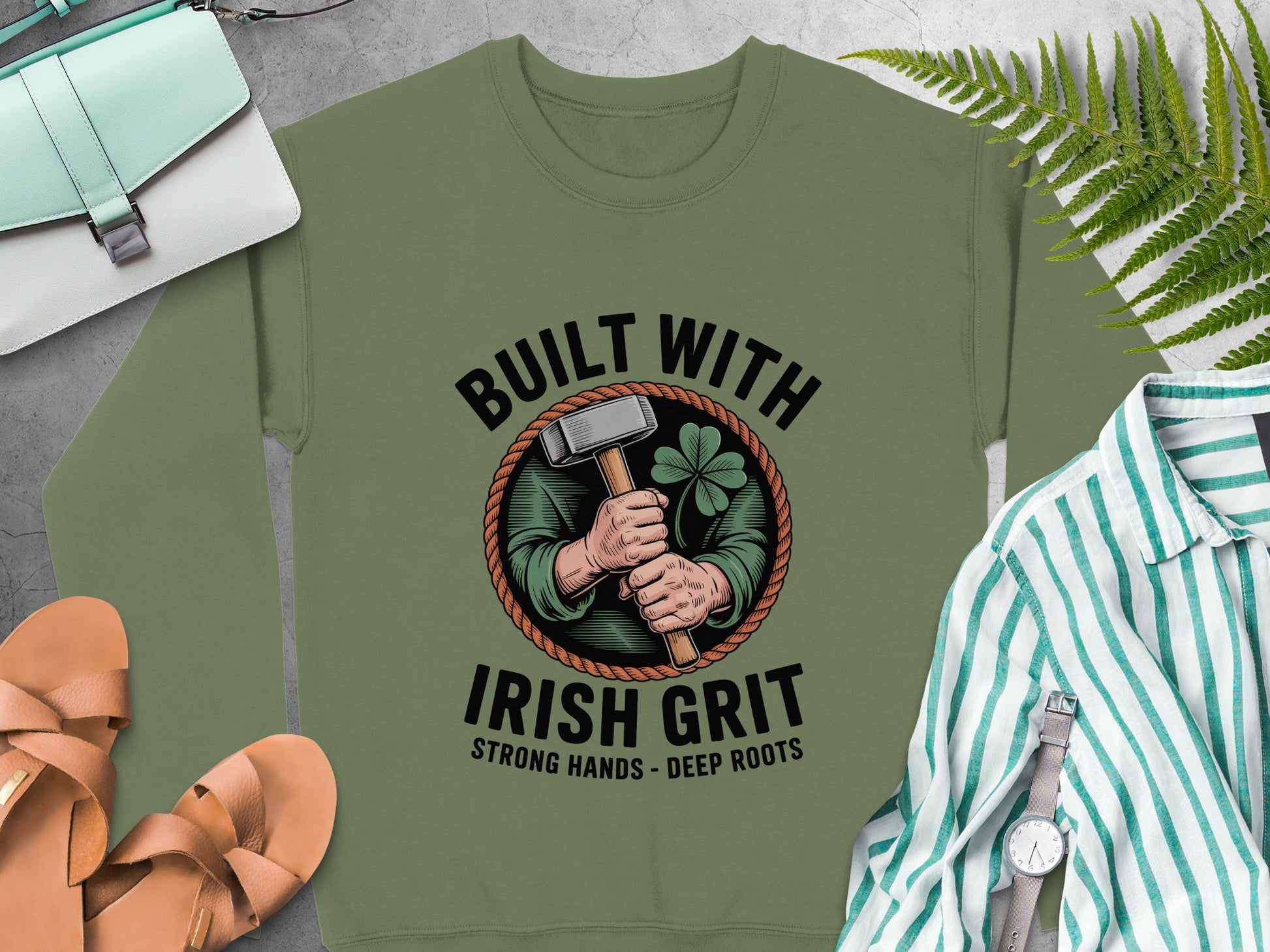 "Built with Irish Grit" graphic of hands holding a hammer and shamrock on Military Green sweatshirt